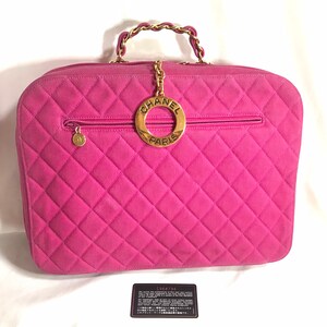 May include: A pink quilted Chanel handbag with a gold chain strap and a circular gold logo with the text "CHANEL PARIS".