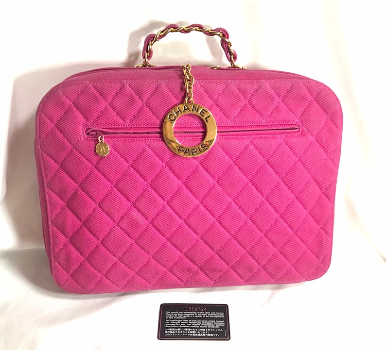 May include: A pink quilted Chanel handbag with a gold chain strap and a circular gold logo with the text "CHANEL PARIS".