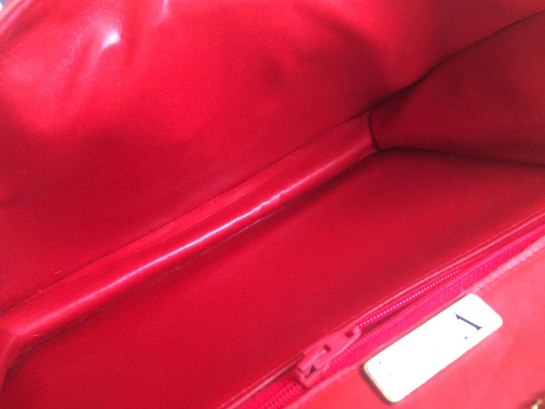 May include: The inside of a red handbag with a zipper and a white tag with the number "1" on it.