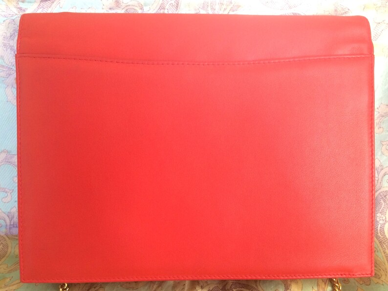 May include: A bright red leather clutch bag with a gold chain strap.