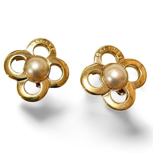 Puede incluir: Un par de pendientes de tono dorado con un diseño de trébol de cuatro hojas y una perla en el centro de cada trébol. Los pendientes están marcados con "CELINE" en la parte posterior.
