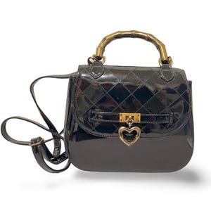 May include: Black patent leather handbag with a quilted pattern. Features a bamboo handle and a gold-tone heart-shaped clasp. Includes a detachable shoulder strap. A stylish accessory.