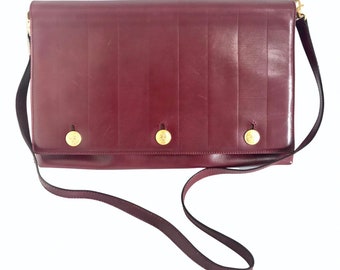 May include: A burgundy leather shoulder bag with a long strap and three gold buttons.