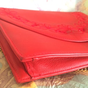 May include: A red leather clutch purse with a gold chain strap and floral embroidery.