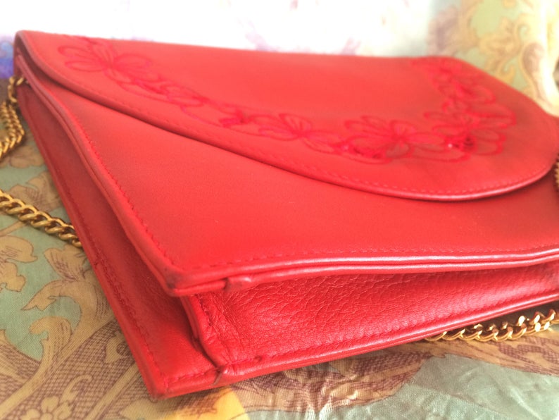 May include: A red leather clutch purse with a gold chain strap and floral embroidery.