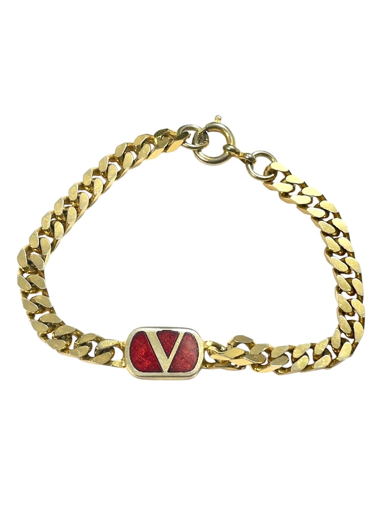 K&ouml;nnte beinhalten: Goldfarbenes Kettenarmband mit einem rechteckigen roten Emaille-Akzent und einem wei&szlig;en V-f&ouml;rmigen Logo. Das Armband hat ein klassisches Panzerketten-Design und einen sicheren Verschluss.