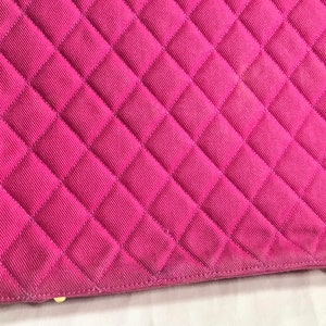 May include: Close-up of a pink quilted fabric handbag. The fabric has a diamond pattern and is stitched with a light pink thread.