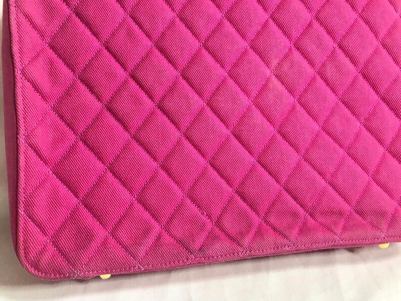 May include: Close-up of a pink quilted fabric handbag. The fabric has a diamond pattern and is stitched with a light pink thread.