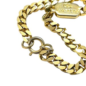 K&ouml;nnte beinhalten: Nahaufnahme einer goldfarbenen Halskette mit einem klobigen Panzerketten-Design. Die Halskette hat einen Verschluss und ein rechteckiges Etikett mit dem eingravierten Markennamen "valentino". Der Schmuck ist vor einem wei&szlig;en Hintergrund platziert.