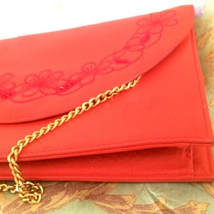 May include: A bright orange leather clutch purse with a gold chain strap and a floral design.