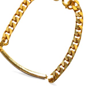 K&ouml;nnte beinhalten: Ein goldfarbenes Kettenarmband mit einem Curb-Link-Design. Das Armband hat einen rechteckigen Steg in der Mitte und einen Verschluss. Der Schmuck wird vor einem wei&szlig;en Hintergrund pr&auml;sentiert.