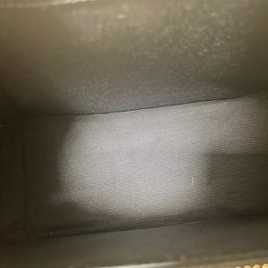 Puede incluir: Vista interior de un bolso negro. El interior est&aacute; forrado con una tela gris a rayas horizontales. El interior del bolso es oscuro, con la fuente de luz desde arriba.