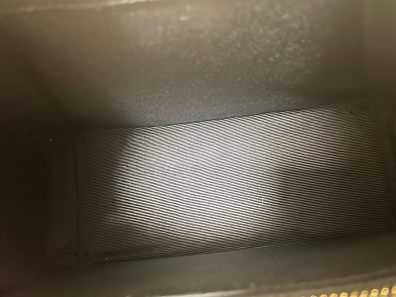 Puede incluir: Vista interior de un bolso negro. El interior est&aacute; forrado con una tela gris a rayas horizontales. El interior del bolso es oscuro, con la fuente de luz desde arriba.