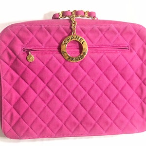 May include: A pink quilted Chanel handbag with a gold chain strap and a circular gold logo with the text "CHANEL PARIS".