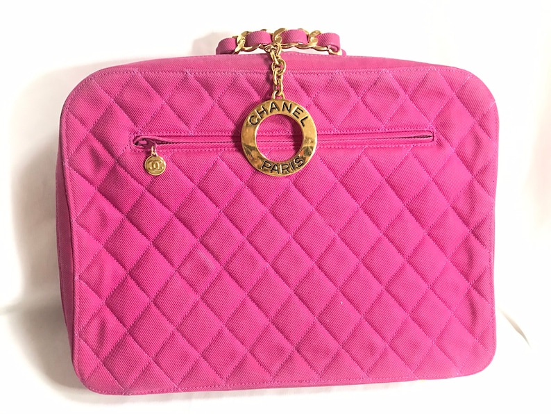 May include: A pink quilted Chanel handbag with a gold chain strap and a circular gold logo with the text "CHANEL PARIS".