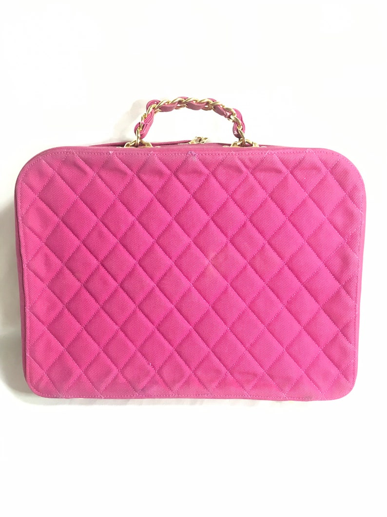 May include: A pink quilted handbag with a gold chain handle.