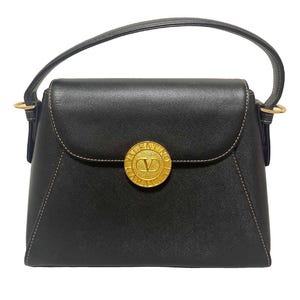 Puede incluir: Bolso de mano negro con solapa superior curvada y un emblema circular dorado. El emblema presenta la letra "V" dentro de un c&iacute;rculo. El bolso tiene un asa superior y herrajes dorados.