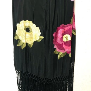 May include: Black silk shawl with embroidered flowers in shades of pink, yellow, and purple. The shawl has black fringe.