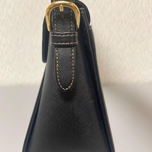 Puede incluir: Bolso de mano negro con forma trapezoidal estructurada. Cuenta con una hebilla dorada y detalles de costura. El asa es negra con costuras doradas a juego. El bolso tiene un dise&ntilde;o cl&aacute;sico y elegante.