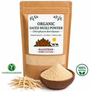 May include: A brown paper pouch containing organic Safed Musli powder, labeled with text including Chlorophytum Borivilianum and Rajasthan Herbs Culture. A wooden bowl filled with the beige powder and a pile of dried roots sit in front of the pouch.