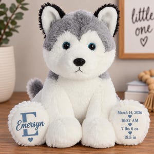 May include: A plush husky stuffed animal with grey and white fur, blue eyes, and a black nose. The left foot features a large blue letter E with the name Emersyn and a heart. The right foot displays March 14, 2026, 10:27 AM, 7 lbs 6 oz, 19.5 in.