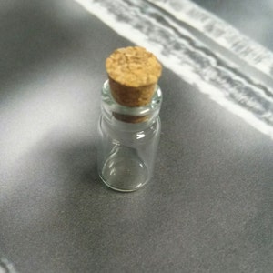 May include: A small, clear glass bottle with a cork stopper. The bottle is empty and has a round shape.