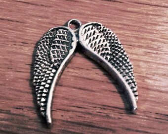 May include: Silver angel wings charm with a detailed design. The wings are connected at the top with a loop for attaching to a necklace or bracelet.