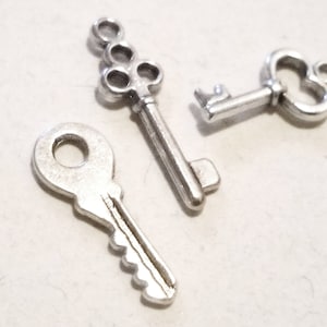 May include: Three silver-toned key charms. One key charm has a heart-shaped bow, another has a round keyhole, and the third has a decorative keyhole with multiple loops.