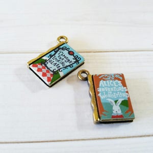 May include: Two antique gold-toned book charms. One charm features a blue and white book with the title "Through the Looking Glass". The other charm features a brown and blue book with the title "Alice's Adventures in Wonderland".