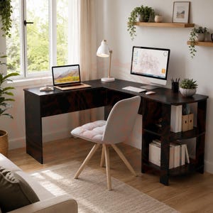 May include: An L-shaped black desk with integrated side shelving, a light grey upholstered chair with wooden legs, a laptop, a computer monitor, a white desk lamp, and various office supplies arranged on the surface and shelves.