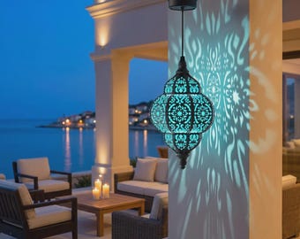 May include: A hanging metal lantern with a dark finish and intricate cut-out patterns that project a bright teal light onto a nearby pillar. The lantern features a rounded, bulbous shape and is suspended by a thin wire from a small solar panel.