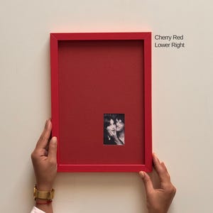 Puede incluir: Un marco de fotos rectangular de color rojo cereza con un paspartú rojo a juego. Una pequeña fotografía en blanco y negro de dos personas está centrada en la parte inferior derecha. El texto Cherry Red Lower Right está impreso en negro.