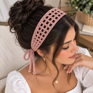 May include: A dusty rose crochet headband featuring an openwork grid pattern. The headband is tied at the side with two thin, dangling crochet cords that end in small, rounded knots, securing the accessory around the head with a soft texture.