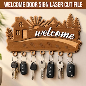 May include: A laser-cut wooden wall-mounted key holder featuring a house, sun, mountains, and pine trees. The word "welcome" is written in white script. The lower section displays engraved footprints and seven metal rings holding various keys.