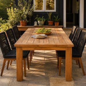 Puede incluir: Una mesa de comedor rectangular para exteriores hecha de madera marrón claro con una superficie de listones, acompañada de seis sillas con marcos de madera y asientos tejidos en negro. Un cuenco poco profundo con plantas verdes está en el centro.