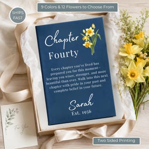 Peut inclure: Une boîte cadeau rectangulaire bleu marine avec le texte Chapter Fourty, une illustration de jonquilles jaunes, le prénom Sarah et Est. 1956. La boîte porte une citation sur les chapitres de la vie et est présentée dans du papier de soie.