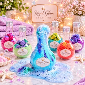 May include: Five glass bottles filled with colourful bath salts and a central, overflowing blue bath bomb, all featuring Royal Glam Creations labels. The scene includes scattered bath salts, a starfish, and floating bubbles.