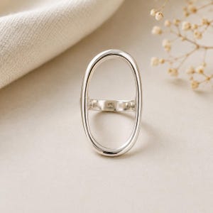 Könnte beinhalten: Ein polierter Silberring mit einem großen, vertikalen, ovalen, offenen Rahmendesign. Das Band ist glatt und abgerundet, wobei der Stempel 925 auf der Innenseite des Rings deutlich sichtbar ist, was auf eine Fertigung aus Sterlingsilber hinweist.