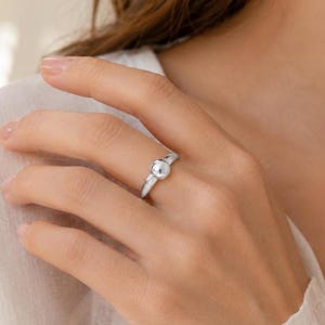 May include: A polished silver ring featuring a single, smooth, spherical bead centered on a slender, rounded band. The metal has a reflective, high-shine finish that catches the light, creating a clean and simple design for the finger.