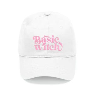 May include: A white baseball cap featuring the embroidered text Basic Witch in a light pink cursive font. The design includes a small bat icon positioned above the word Basic. The cap has a structured crown, a curved brim, and a button on top.