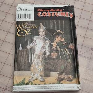 May include: A Simplicity Costumes sewing pattern envelope for The Wizard of Oz, featuring illustrations of a Tin Man costume in metallic silver fabric and a Scarecrow costume with straw accents. The package includes the pattern number 7814.