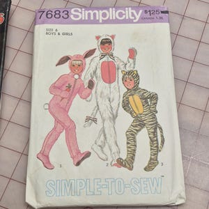 Peut inclure: Une pochette de patron de couture Simplicity 7683 pour costumes taille 6 garçons et filles. La couverture présente des illustrations de trois enfants portant des costumes d'animaux : un lapin rose, un chat blanc à ventre rose et un tigre rayé jaune et noir.