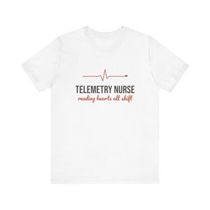 May include: A white short-sleeved t-shirt featuring a red EKG heart rhythm line graphic above the text TELEMETRY NURSE in dark gray capital letters, followed by the red cursive script text reading hearts all shift centered on the chest.