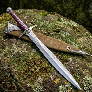 Può includere: Una spada in metallo color argento con una lama appuntita caratterizzata da incisioni a volute e una punta affilata. L'impugnatura è avvolta in materiale bordeaux scuro con accenti argentati. È accompagnata da un fodero in camoscio color cuoio.