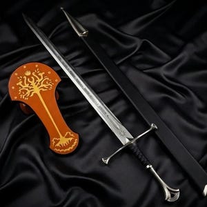 Può includere: Una spada in metallo argentato con impugnatura avvolta in nero e guardia, accompagnata da un fodero nero con accenti argentati e una placca espositiva in legno arancione con un disegno di un albero dorato sormontato da una corona.