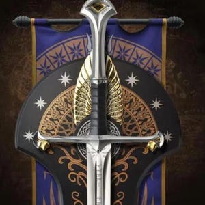 May include: A silver sword with a black grip and gold accents mounted on a black and purple shield-shaped plaque. The sword features a pointed pommel, a crossguard with gold tips, and etched runes on the blade. The plaque displays star motifs.