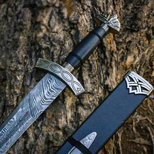 Peut inclure: Une épée avec une lame en acier damas à motifs, un manche noir et une garde argentée ornée d'un motif de nœuds gravé. L'épée est accompagnée d'un fourreau noir doté de garnitures métalliques argentées à l'extrémité et à la base.