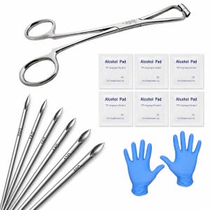 May include: A stainless steel piercing clamp, six silver piercing needles marked 20G, 18G, 16G, 14G, 12G, and 10G, six white square alcohol pad packets labelled 70% Isopropyl Alcohol, and a pair of blue nitrile gloves for medical or body piercing use.