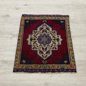 Peut inclure: Un tapis rectangulaire présentant un champ rouge profond avec un médaillon central en forme de losange géométrique crème et bleu. La bordure affiche un motif répétitif en or, bleu et rouge, avec des franges courtes sur les bords supérieur et inférieur.