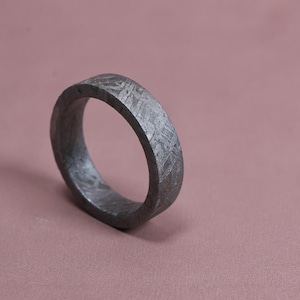 May include: A dark gray ring with a textured surface featuring a distinct cross-hatched, crystalline pattern. The band has a flat profile and a matte finish, showcasing a metallic appearance with intricate geometric lines etched across the exterior.